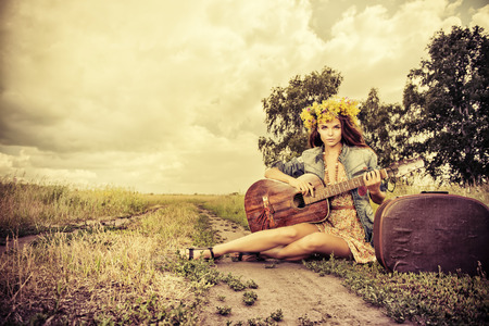Romantic girl in a wreath of wild flowers travelling with her guitar. Summer. Hippie style.の写真素材
