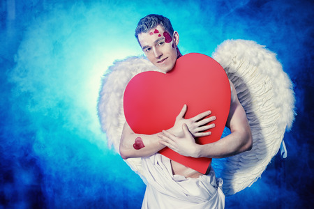 Romantic male Angel Cupid standing with big red heart and smiling at camera. Valentine's day. Love concept.の写真素材