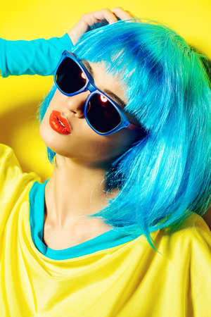 Bright glamorous girl in vivid clothes and a wig alluring over yellow . Beauty, fashion. Cosmetics, hairstyle. Optics, eye wear.の写真素材