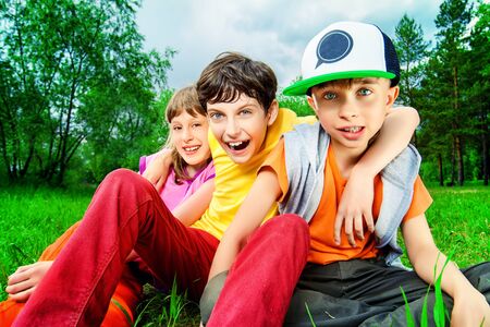 Three joyful children sitting on the grass in the park. Summer.の写真素材