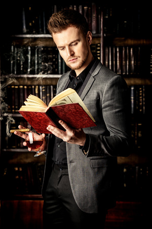 Elegant man in a suit with glass of beverage stands in vintage room. Fashion.の写真素材