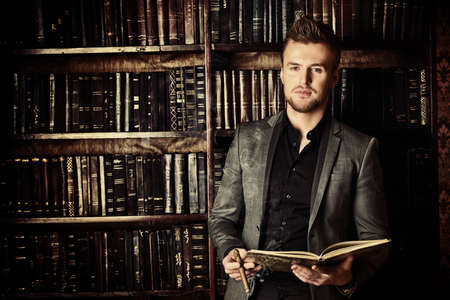Handsome well-dressed man stands by bookshelves in a room with classic interior. Fashion.の写真素材