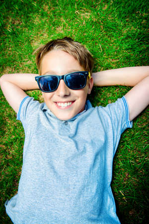 Cool boy lying on a grass at a park and smiles. Summer day. Holiday.の写真素材