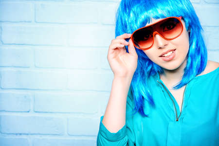 Fashion girl in bright blue wig and sunglasses posing by the urban white brick wall. Beauty, fashion.の写真素材