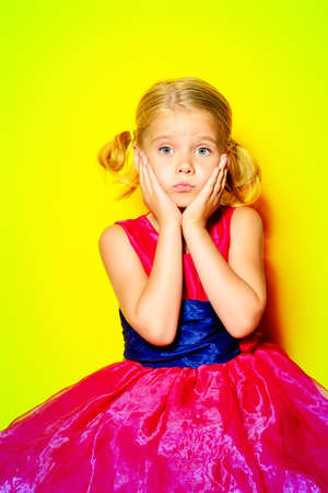 Pretty little girl posing in bright pink dress over yellow background.の写真素材