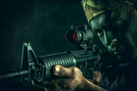 A soldier in war paint looks through the scope of automatic rifles.の写真素材