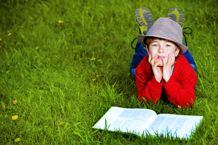 Cute 7 years old boy lying on a grass with a book. Summer day.の写真素材