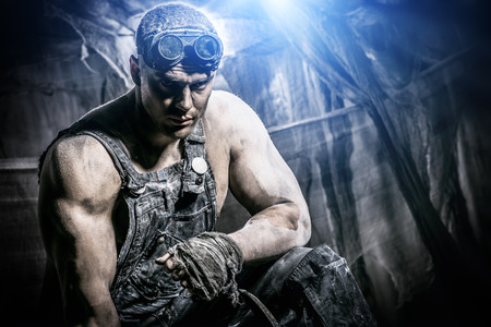 Portrait of a strong muscular man coal miner standing over dark grunge background. Mining industry. Art concept.の写真素材
