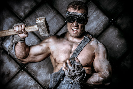 Strong aggressive coal miner with a hammer over dark grunge background. Mining industry. Art concept.の写真素材