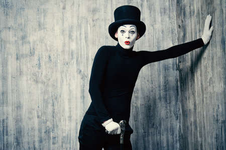 Elegant expressive male mime artist posing with walking stick by a grunge wall.の写真素材