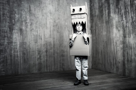 Black-and-white portrate of a dreamer boy playing with a cardboard dragon, dinosaur. Childhood....
