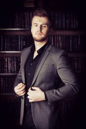 Handsome well-dressed man stands by bookshelves in a room with classic interior. Fashion.の写真素材