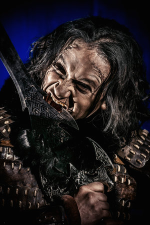Close-up portrait of the ancient male warrior in armor holding sword. Historical character. Fantasy.