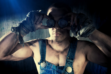 Brutal muscular dirty man in goggles over dark grunge background. Mining industry. World of the future, Apocalypse.の写真素材