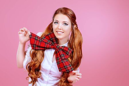 Portrait of a pretty smiling teen girl in school uniform posing over pink background. Anime style.の写真素材