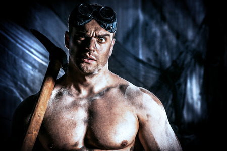 Muscular dirty coal miner with a pickaxe over dark grunge background. Mining industry. Art concept.の写真素材