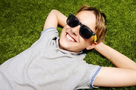 Cool boy lying on a grass at a park and smiles. Summer day. Holiday.の写真素材