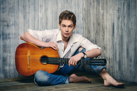 Romantic young man playing an acoustic guitar, sitting on the wooden floorの写真素材