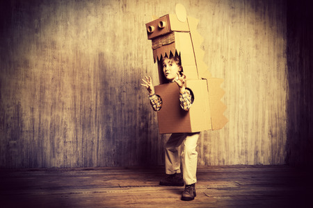 Funny dreamer boy playing with a cardboard dragon, dinosaur. Childhood. Fantasy, imagination. Retro style, sepia.の写真素材
