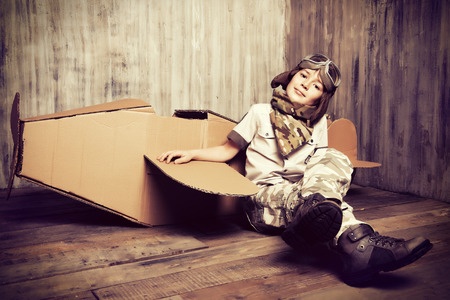 Cute dreamer boy playing with a cardboard airplane. Childhood. Fantasy, imagination. Retro style.の写真素材