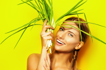 Joyful young woman with green onion over summer yellow background. Healthy food.の写真素材