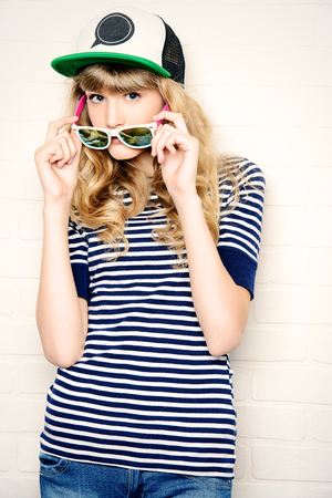 Joyful teen girl in casual clothes and sunglasses posing by a brick wall. Active lifestyle. Youth fashion. Studio shot.の写真素材