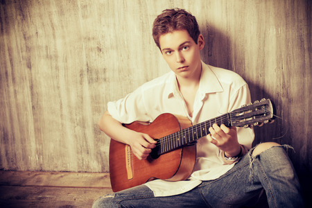 Romantic young man playing an acoustic guitar, sitting on the wooden floorの写真素材