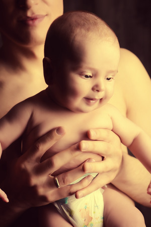 Lovely little baby on the father's hands. Safety and care concept. Happy childhood. Studio shot over black background.の写真素材