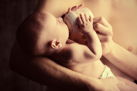 Caring father feeding his baby from a bottle. Healthy baby food and infant formula, milk. Studio...