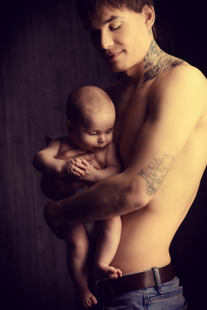 Lovely little baby on the father's hands. Safety and care concept. Happy childhood. Studio shot over black background.の写真素材