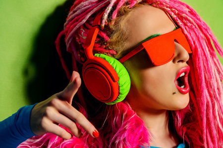 Modern party girl DJ in bright clothes, headphones and with bright dreadlocks. Disco, party. Show...