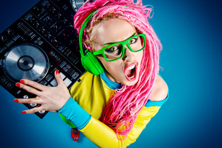 Expressive modern DJ girl wearing bright clothes, headphones and bright dreadlocks mixing up some...