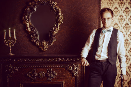 Young handsome man in evening suit stands by the fireplace in a room with classic vintage interior. Fashion.の写真素材