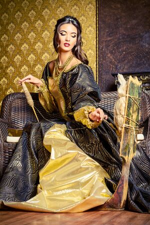 Beautiful fairy girl like a Snow White in a beautiful lush dress spins on the spinning wheel.  Renaissance. Barocco. Fashion. Fairy tale.の写真素材