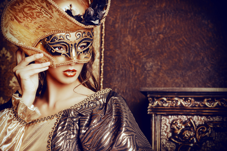 Venetian masquerade carnival. Elegant lady wearing beautiful lush dress and venetian mask stands in a palace room. Renaissance. Barocco. Fashion.の写真素材