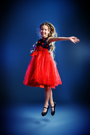 Cute teen girl in a beautiful festive dress dancing at studio. Beauty, children's fashion. Studio shot.の写真素材