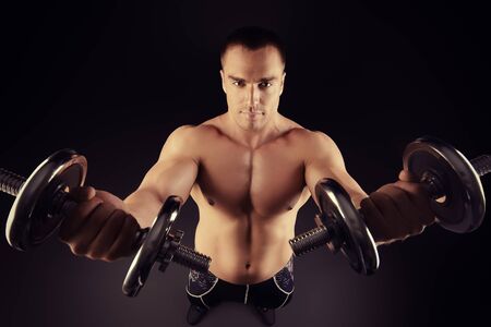 Handsome muscular man posing with dumbbells over black background. Bodybuilding. Professional sports.の写真素材