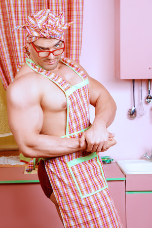 Handsome muscular man in an apron cooking in the pink kitchen. Love concept. Valentine's day.の写真素材