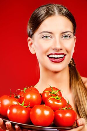 Beautiful smiling young woman holding a dish with ripe juicy tomatoesの写真素材