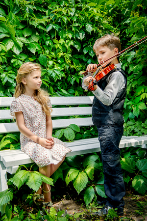 Romantic young violinist playing the violin for pretty little girl at a parkの写真素材