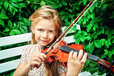 Pretty little girl playing the violin at a summer park.の写真素材