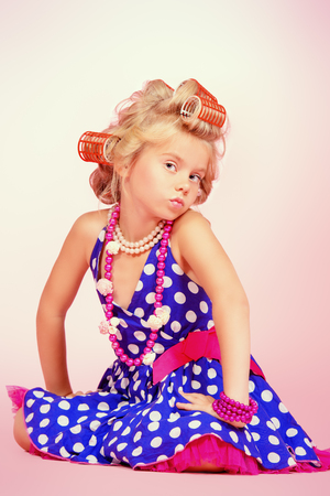 Beautiful little girl in her mother\'s hair curlers and polka-dot dressの写真素材