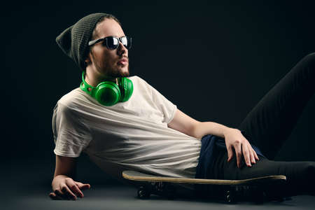 Young man in hat sitting on his skateboard over black background.の写真素材
