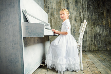 Romantic little girl in white dress playing the piano. Music and art concept. Retro style.の写真素材