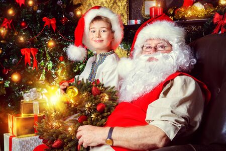Santa Claus in his everyday clothes in Christmas home décor. Happy little boy helps Santa Claus get ready for Christmas.の写真素材
