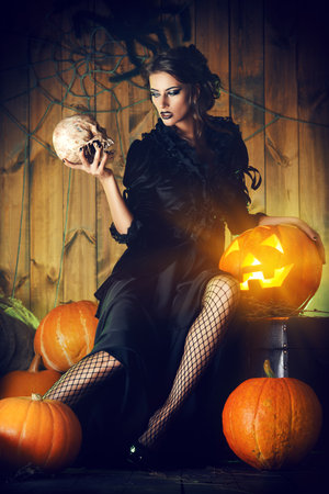 Attractive witch girl in black dress holding a skull in a mysterious abandoned house. Witchcraft, witch. Vampire.  Halloween concept.の写真素材