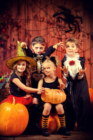 Cheerful children in halloween costumes celebrating halloween in a wooden barn with pumpkins. Halloween concept.の写真素材