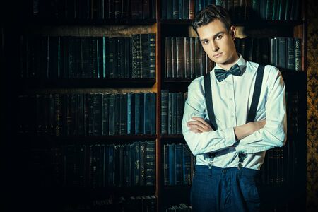 Handsome well-dressed young man stands by bookshelves in a room with classic interiorの写真素材