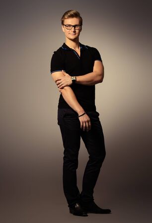 Full length portrait of an attractive masculine man in black clothes posing at studio over grey background.の写真素材