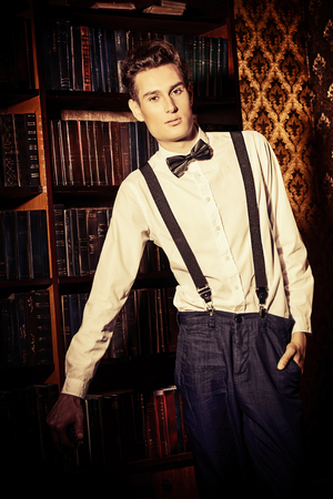 Handsome well-dressed young man stands by bookshelves in a room with classic interior.の写真素材